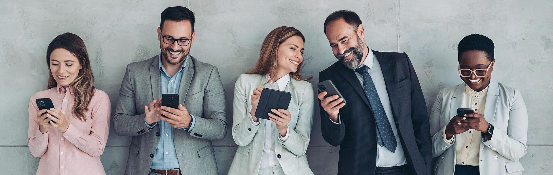 Mehere zufriedene Geschäftsleute nebeneinander mit Handys oder Tablet
