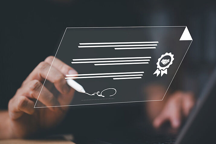 Symbolbild für Digitalisierung im Notariat: Geschäftsmann unterzeichnet am Laptop, digitale Symbole als Grafiken eingeblendet