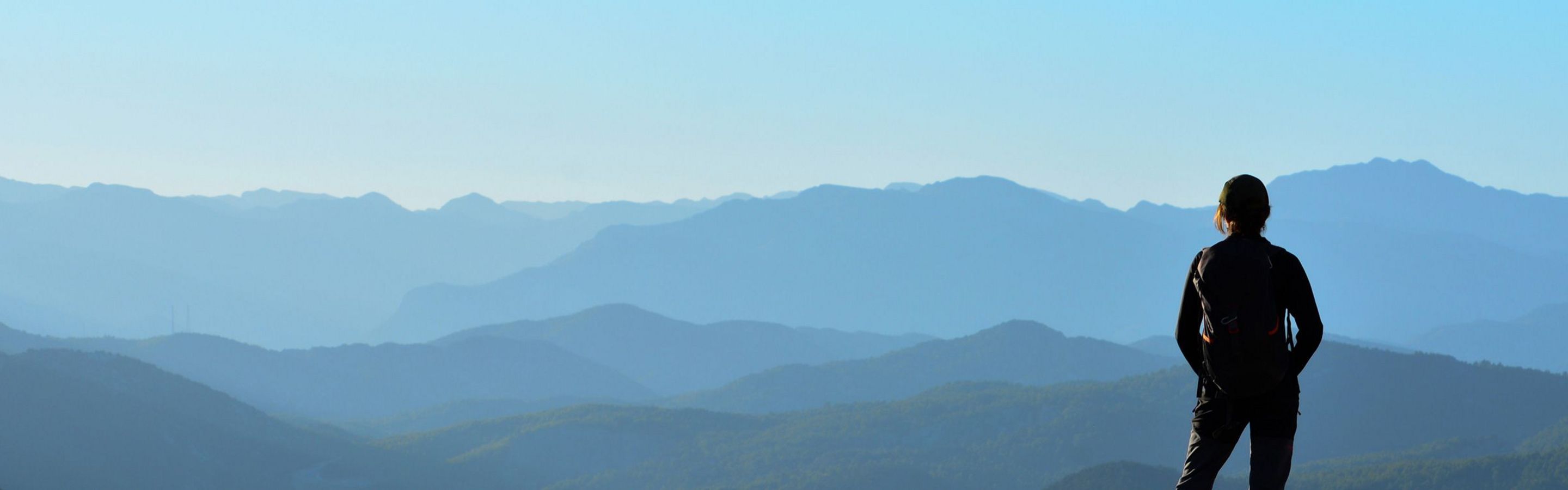 Bild einer Bergsteigerin auf dem Gipfel, die Richtung Horizont blickt