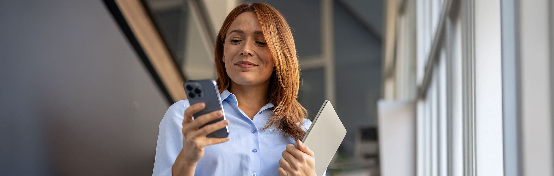 lächelnde Frau mit Laptop sieht auf ihr Handy