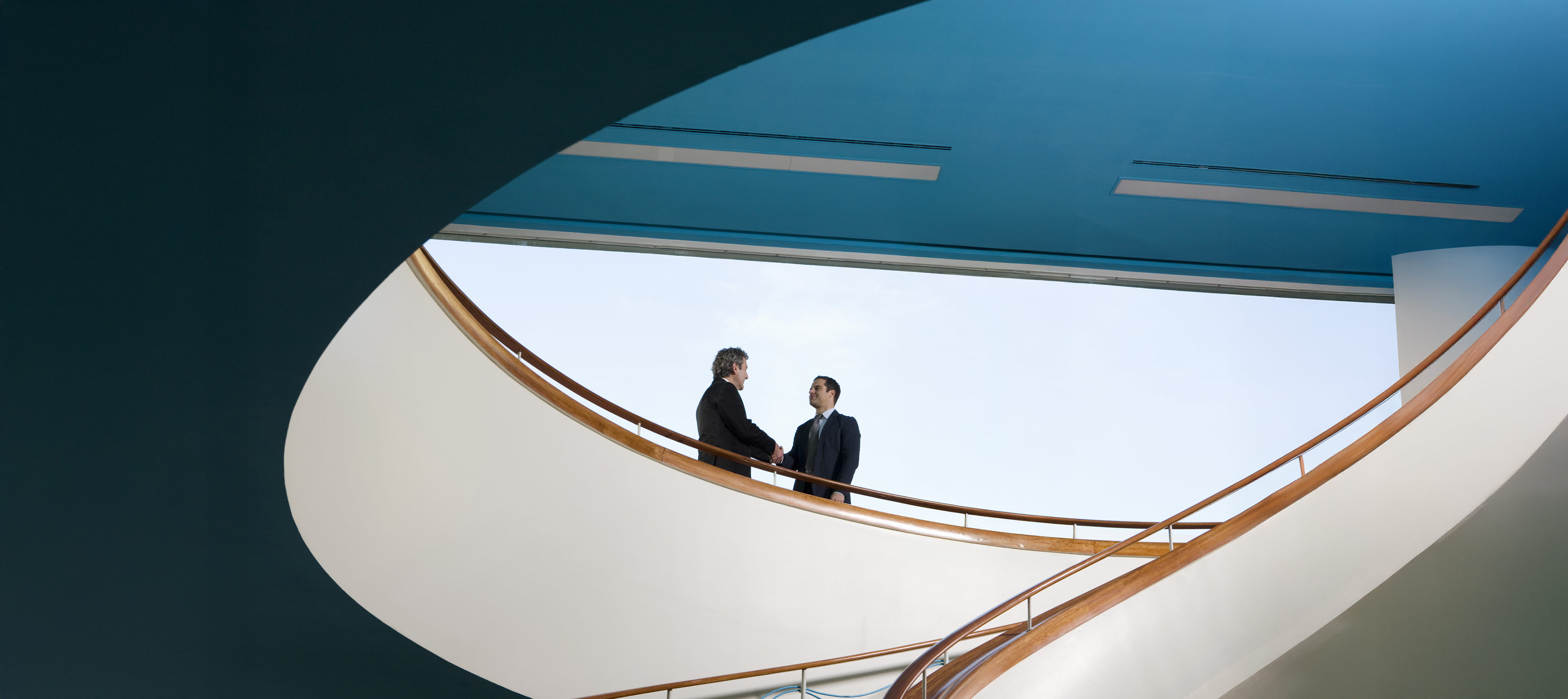 2 Geschäftsmänner in modernen, weitläufigen Treppenhaus geben sich die Hand